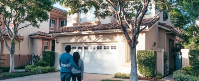 Image of a married couple standing in front of the house they recently bought.